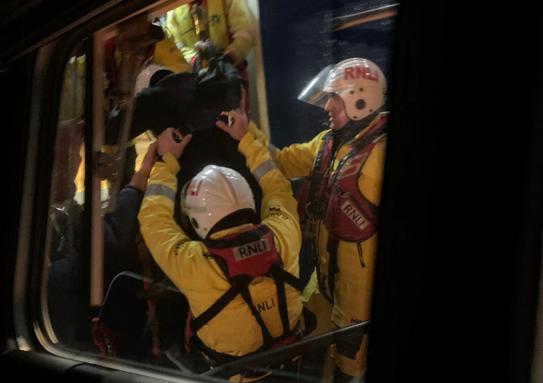 Aberdeen lifeboat crew help the casualty (in dark clothing, but wearing RNLI protective helmet and lifejacket) down the PSV’s pilot ladder and aboard the all-weather lifeboat Bon Accord