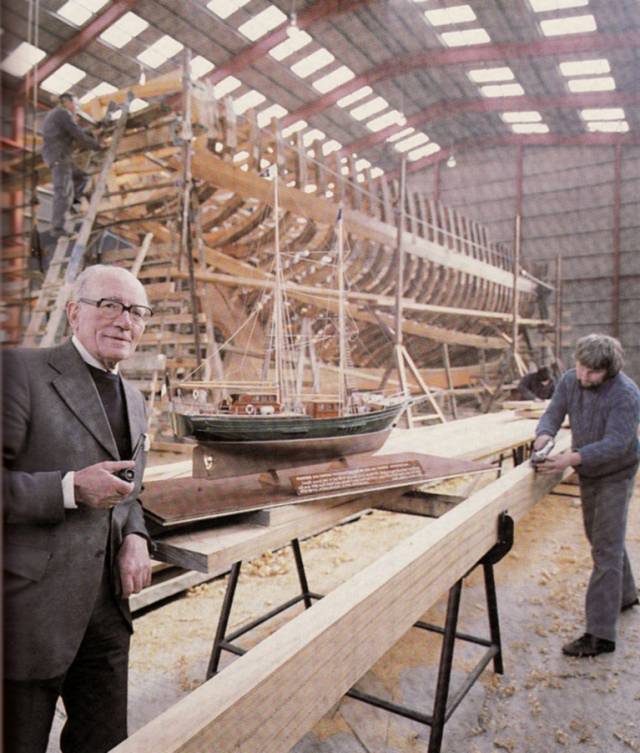 Jack Tyrrell in 1979 the great shed in Arklow in which Asgard II was built. He is seen foreground with the ship’s model which he used to promote the ideal at boat shows and to government ministers, while in the background Asgard II finally takes shape