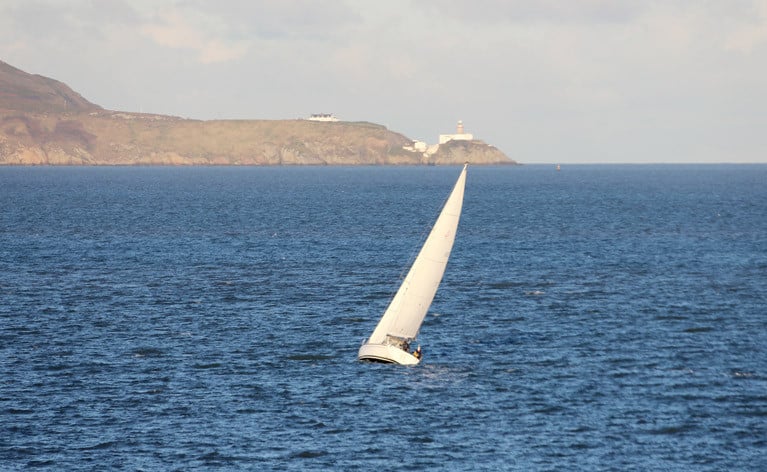 New year sail - A solitary sailing cruiser enjoys a New Year's Day sail on Dublin Bay with Howth's Baily lighthouse in the background
