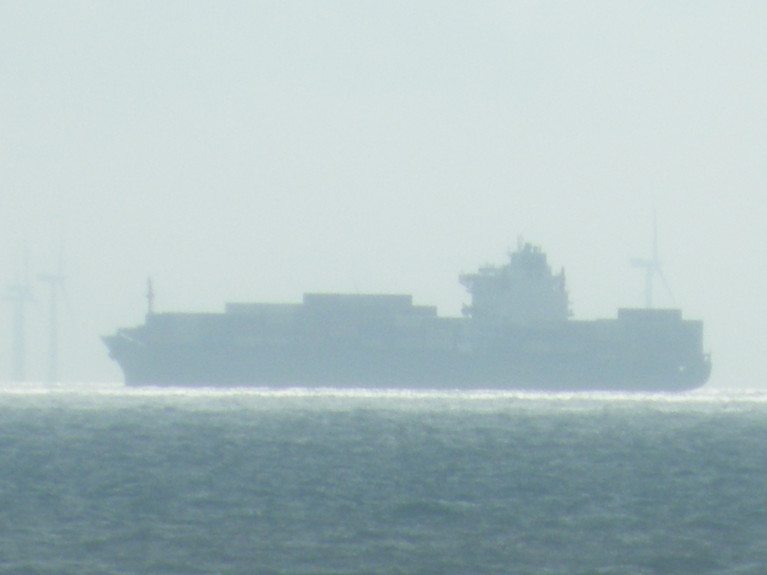 Cutting Emissions: In the UK, radical new climate change commitments will set the country on course to cut carbon emissions by 78% by 2035, the announced was made by the British Government. Above AFLOAT&#039;s photo of a containership in UK waters including wind-farm turbines on the hazy horizon. 