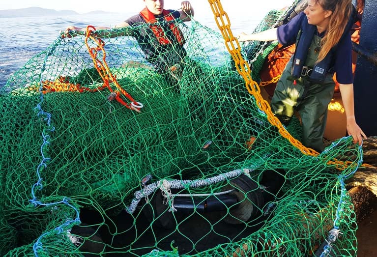 Authors of the study hold up the square mesh panel, inserted into the otter-trawl net with LEDs attached. Lights help to increase escapement of fish through the large square mesh in the panel