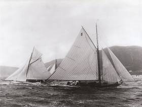 The newly-built Fife-designed Belfast Lough Class I 25ft LWL boats Feltie (George Clark) and Halcyone (Bertie Brown) in action in Clyde Fortnight 1897, just four weeks after they’d had their maiden race on May 29th at Carrickfergus, where they were built by John Hilditch. In a classic Firth of Clyde squall, Feltie is still hanging on to her topsail, though Halcyone under her lowers seems to be providing her robust helmsman with quite enough to be thinking about as he shapes up for a gybe. Belfast Lough Class I made such an impressive debut in Scotland in 1897 that a lengthy report of their success were carried in the New York Times. Photo: Courtesy RUYC